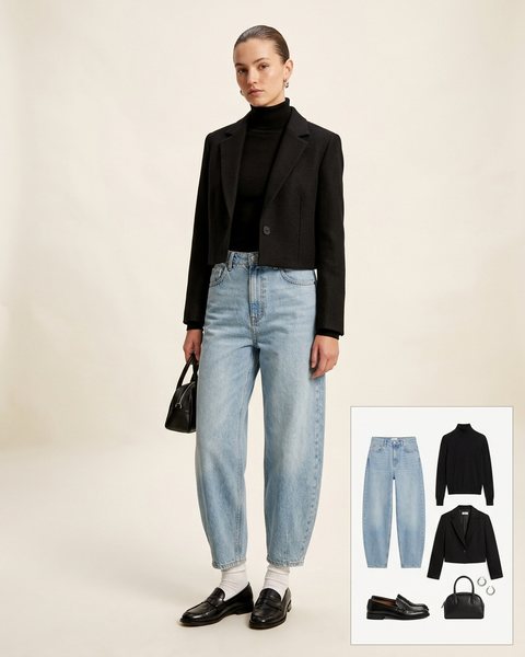 Woman wearing light-wash barrel-leg jeans with a black turtleneck, a cropped black blazer, black loafers with white socks and a black top-handle bag