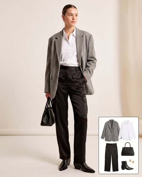 Woman wearing black satin straight-leg cargo pants with a white poplin shirt, an oversized grey wool blazer, pointed black ankle boots and a black top-handle bag