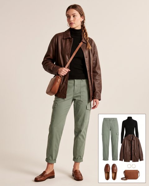 Woman wearing sage green tapered cargo pants with a black ribbed turtleneck, an oversized brown leather jacket, brown penny loafers and a tan crossbody bag