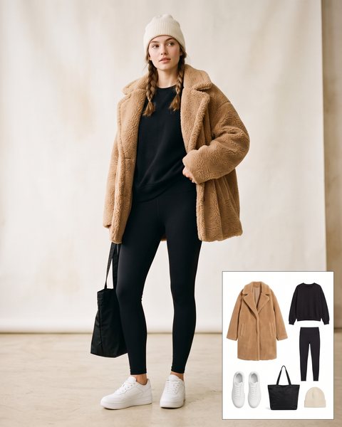 Woman wearing a tan teddy faux fur coat with a black sweatshirt, black leggings, white chunky sneakers, a black tote bag and a cream beanie