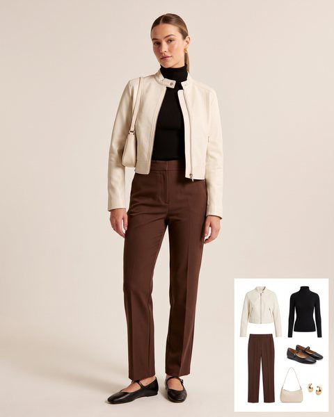 Woman wearing a cream leather moto jacket with a black turtleneck, chocolate brown trousers, black Mary Jane flats and a cream shoulder bag