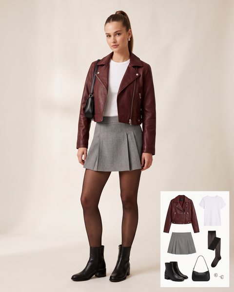 Woman wearing an oxblood leather biker jacket with a white tee, a grey pleated mini skirt, sheer black tights and black ankle boots with a black shoulder bag