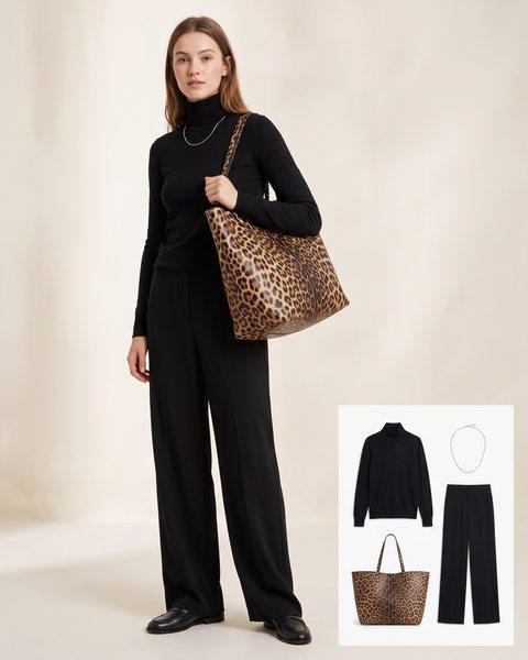 Woman wearing a black turtleneck and black wide-leg trousers with black leather loafers, a silver chain necklace and an oversized leopard print leather tote bag on her shoulder