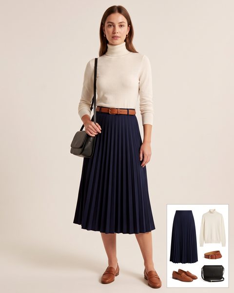 Navy pleated midi skirt with an ivory turtleneck sweater tucked in, a cognac leather belt, cognac loafers and a black crossbody bag