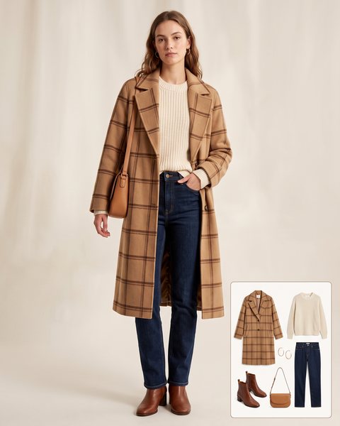 Woman wearing a long camel and brown plaid wool overcoat open over a cream knit sweater with dark-wash straight-leg jeans, brown leather ankle boots and a tan crossbody bag