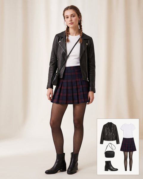 Woman wearing a navy and burgundy plaid pleated mini skirt with a white tee, a black leather biker jacket, sheer black tights, black ankle boots and a black crossbody bag