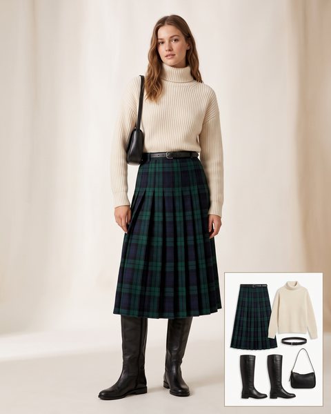 Woman wearing a forest green and navy plaid pleated midi skirt with a cream chunky turtleneck, a black belt, flat black knee-high boots and a black shoulder bag