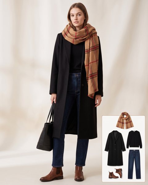 Woman wearing a camel and red plaid blanket scarf with a long black wool coat, a black knit top, dark-wash straight-leg jeans, brown Chelsea boots and a black leather tote bag
