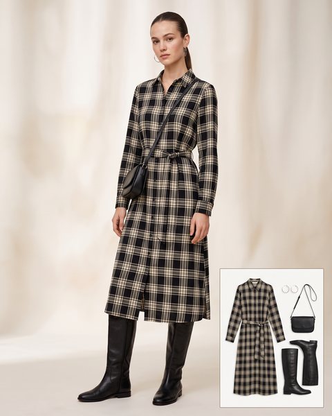 Woman wearing a black and cream plaid belted midi shirt dress with flat knee-high black leather boots, a black crossbody bag and silver hoop earrings