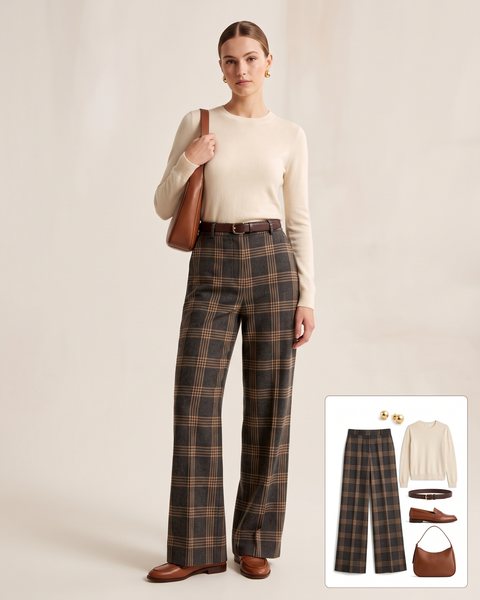 Woman wearing high-waisted charcoal and camel plaid wide-leg trousers with a cream crewneck sweater, a brown leather belt, brown loafers and a brown leather shoulder bag