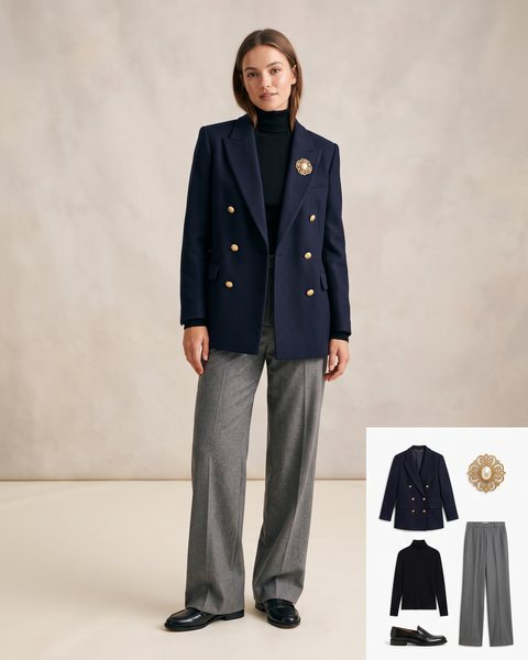 Double-breasted navy blazer with gold buttons and a vintage gold brooch pinned at the lapel, black turtleneck and grey wide-leg trousers