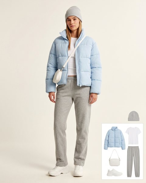 Woman wearing a baby blue short puffer jacket with a white tee, grey sweatpants, chunky white sneakers, a white crossbody bag and a grey beanie