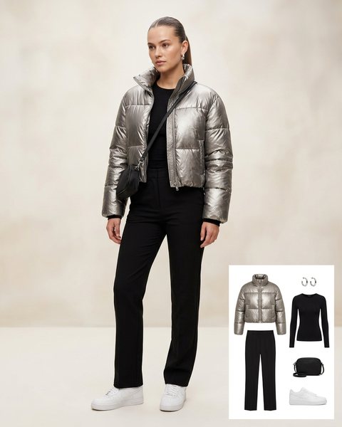 Woman wearing a glossy silver cropped puffer jacket with a black fitted top, black straight trousers, white sneakers and a black crossbody bag