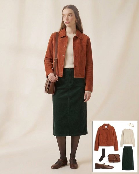 Woman wearing a rust suede cropped jacket with a cream sweater, a dark green corduroy midi skirt, black tights and brown Mary Jane flats