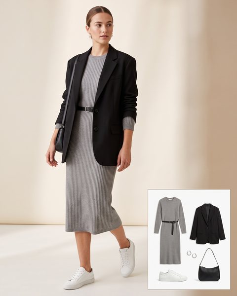 Woman wearing a grey ribbed midi sweater dress with a thin black belt, an oversized black blazer, white leather sneakers and a black shoulder bag