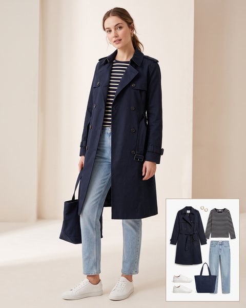 Woman wearing a navy double-breasted trench coat with a striped tee, light-wash jeans, white sneakers and a navy canvas tote