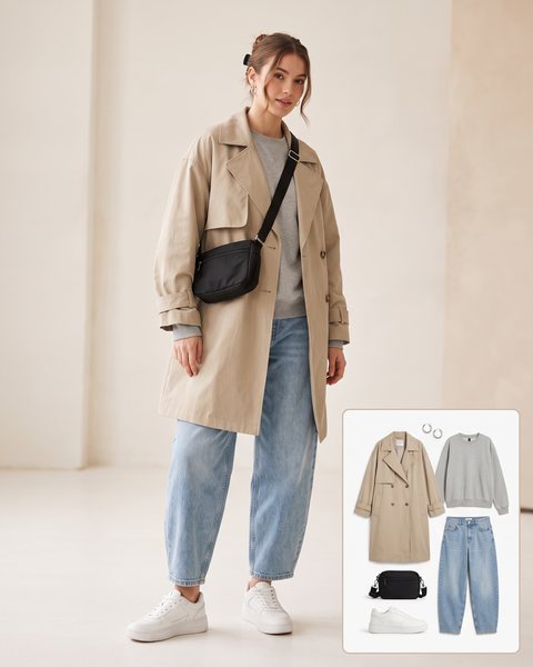 Woman wearing an oversized stone trench coat with a grey sweatshirt, baggy barrel-leg jeans, chunky white sneakers and a black crossbody bag