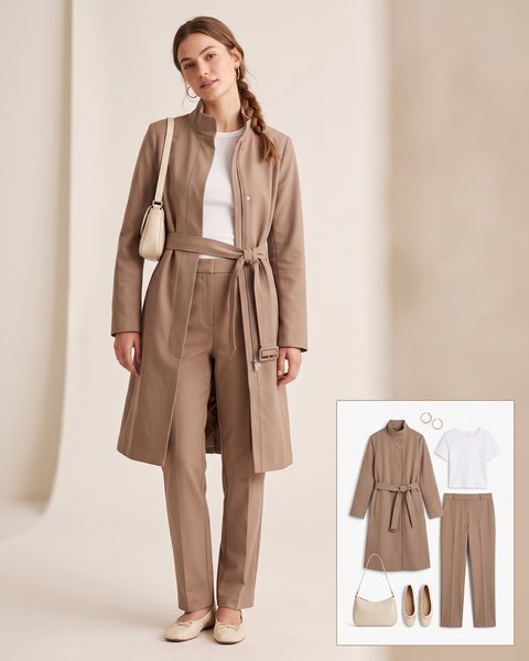 Woman wearing a taupe mock-neck trench coat with a white tee, matching taupe trousers, cream ballet flats and a cream shoulder bag
