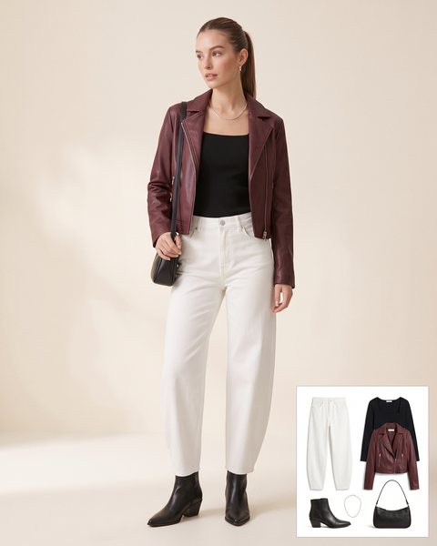 Woman wearing white barrel-leg jeans with a black ribbed square-neck top, a cropped burgundy leather jacket, black pointed ankle boots, a black baguette bag and a silver chain necklace